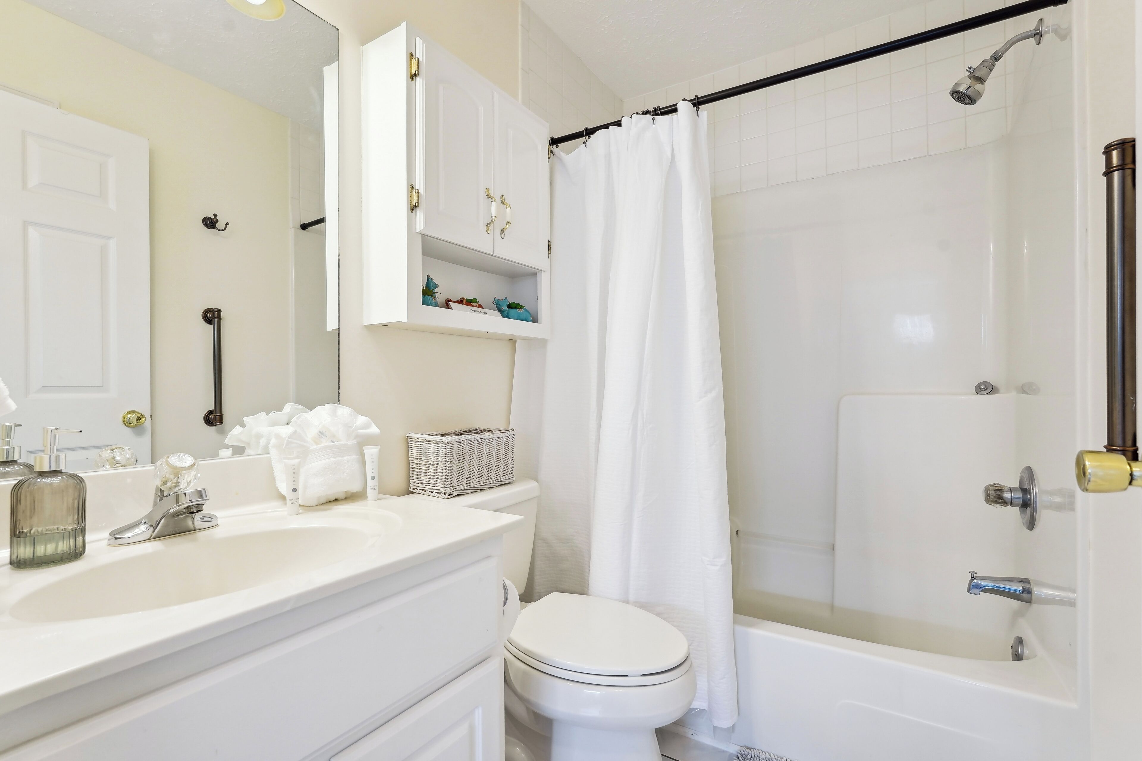 A bathroom with a white sink, toilet, and bathtub. There are white cabinets above the sink and a shower curtain.