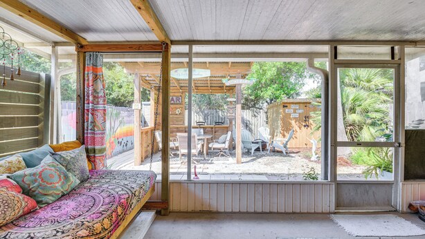 A cozy room with a wooden ceiling, a patterned sofa, and a large window overlooking a backyard with outdoor furniture and a wooden structure. - Breezy PCB Vacation Rental w/ Lanai, Walk to Ocean (Panama City Beach)