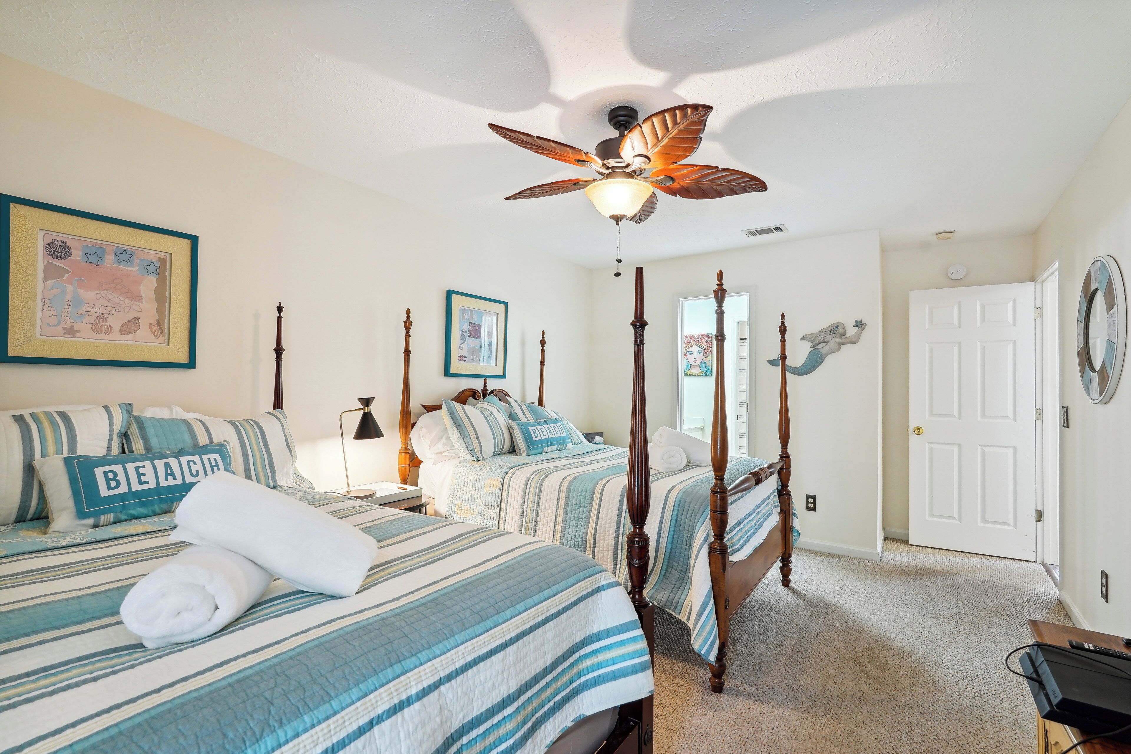 A bedroom with two beds, a ceiling fan, and a door.