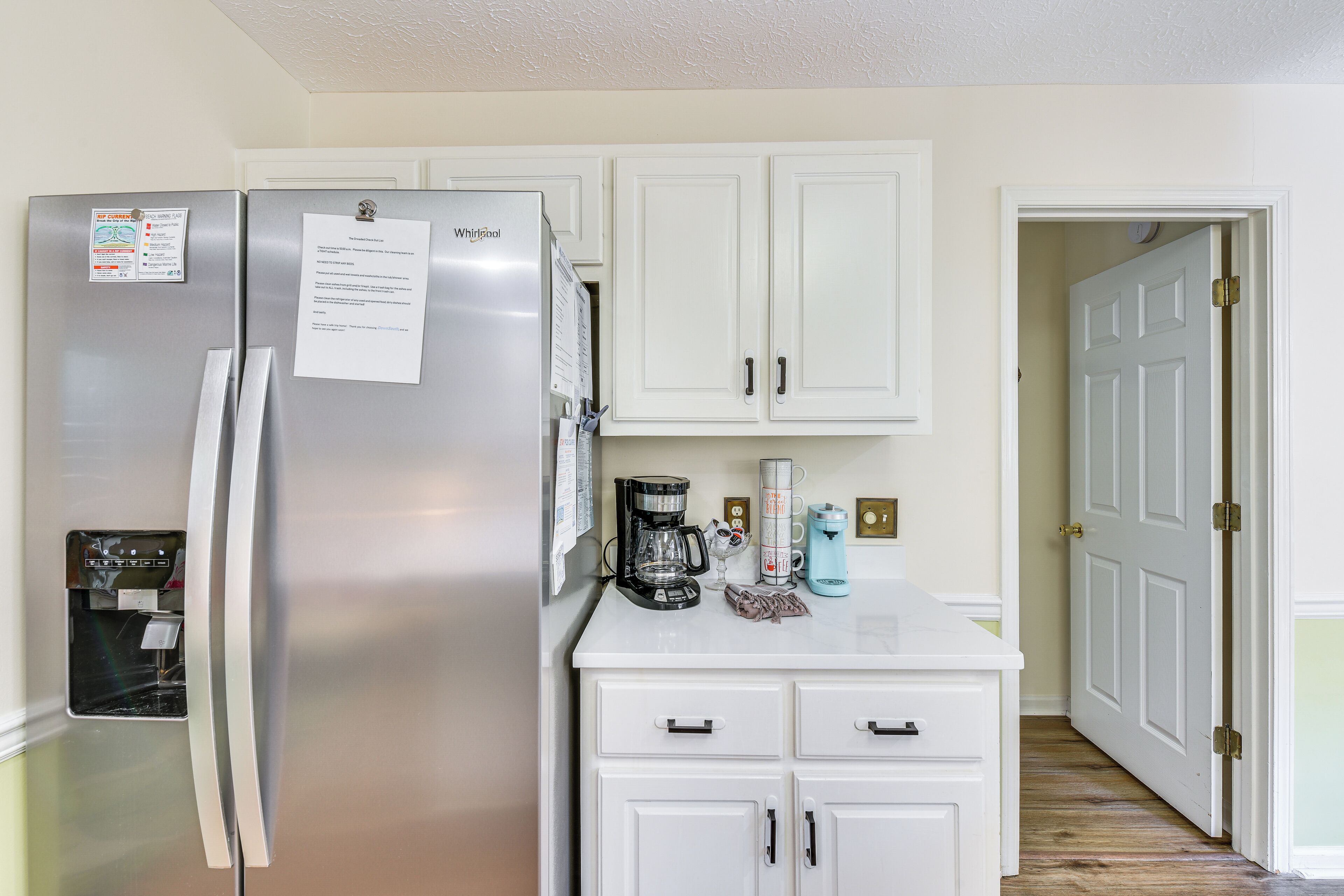A kitchen with a stainless steel refrigerator, white cabinets, a coffee maker, and a water dispenser.