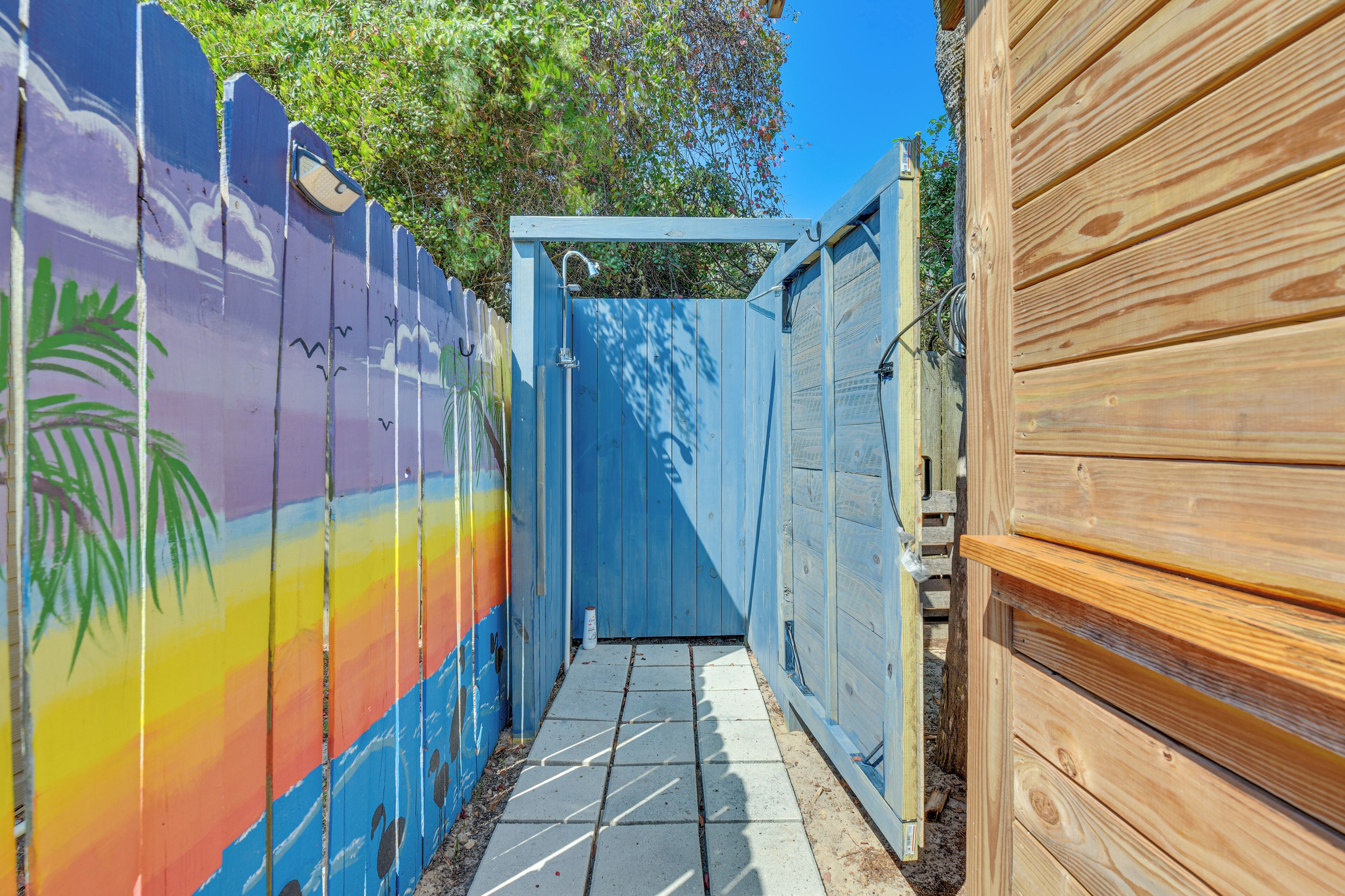 A narrow pathway leading to a blue gate, flanked by a colorful painted fence and a wooden fence.