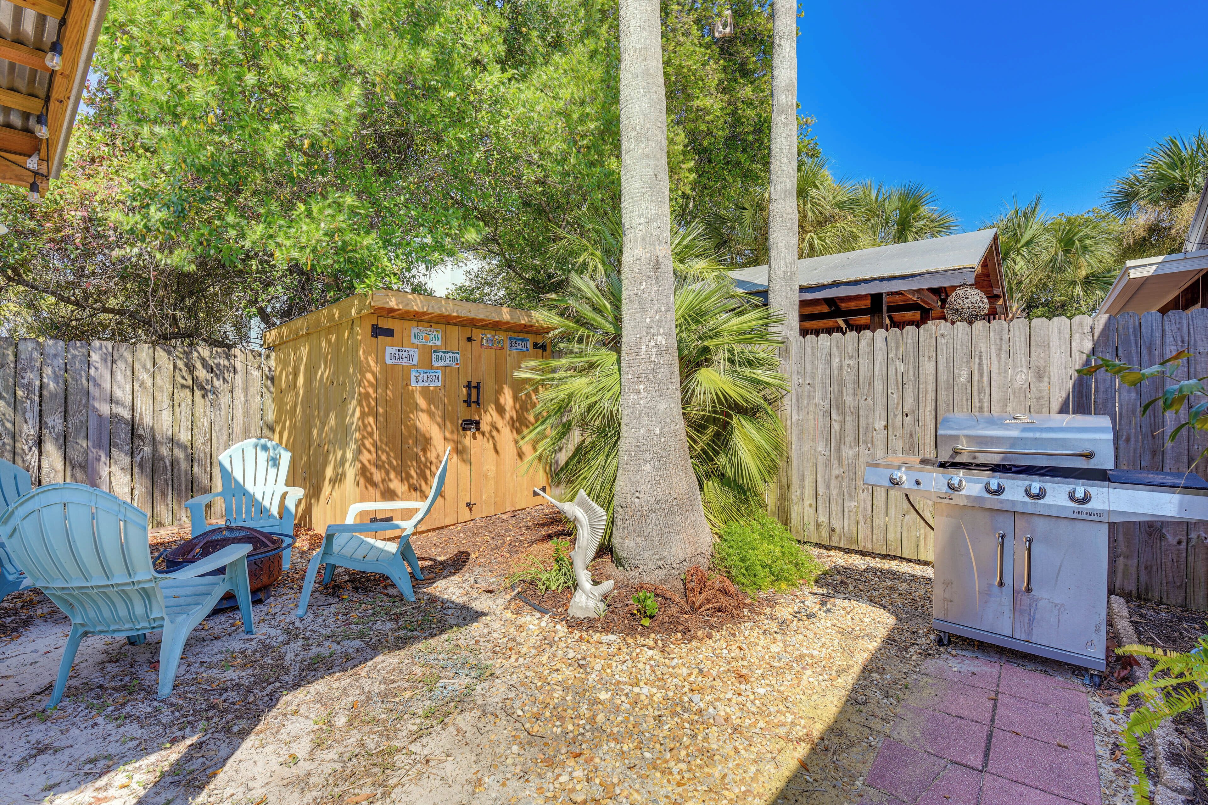 Un jardin avec un barbecue, deux chaises, un abri de jardin en bois et une clôture en bois.