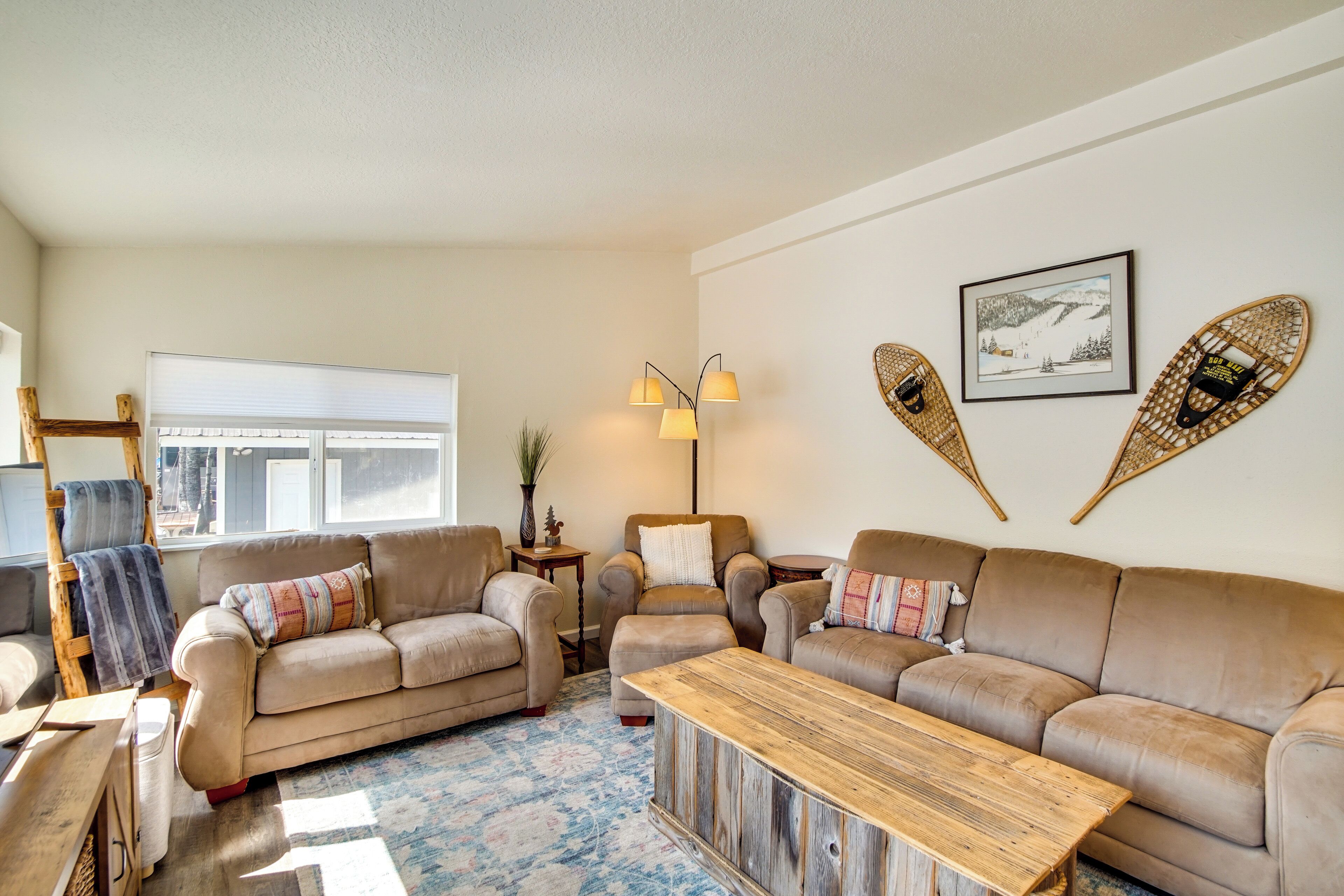 A cozy living room with a beige sofa set, a wooden coffee table, and a large window providing natural light.