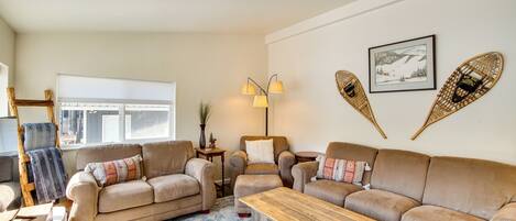 A cozy living room with a beige sofa set, a wooden coffee table, and a large window providing natural light.