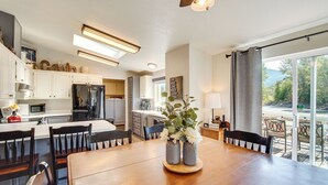 A modern kitchen with white cabinets, a wooden dining table, and a view of the outdoors through large windows. - 18 Mi to Mt Rainier! Family Escape in Packwood (Packwood)