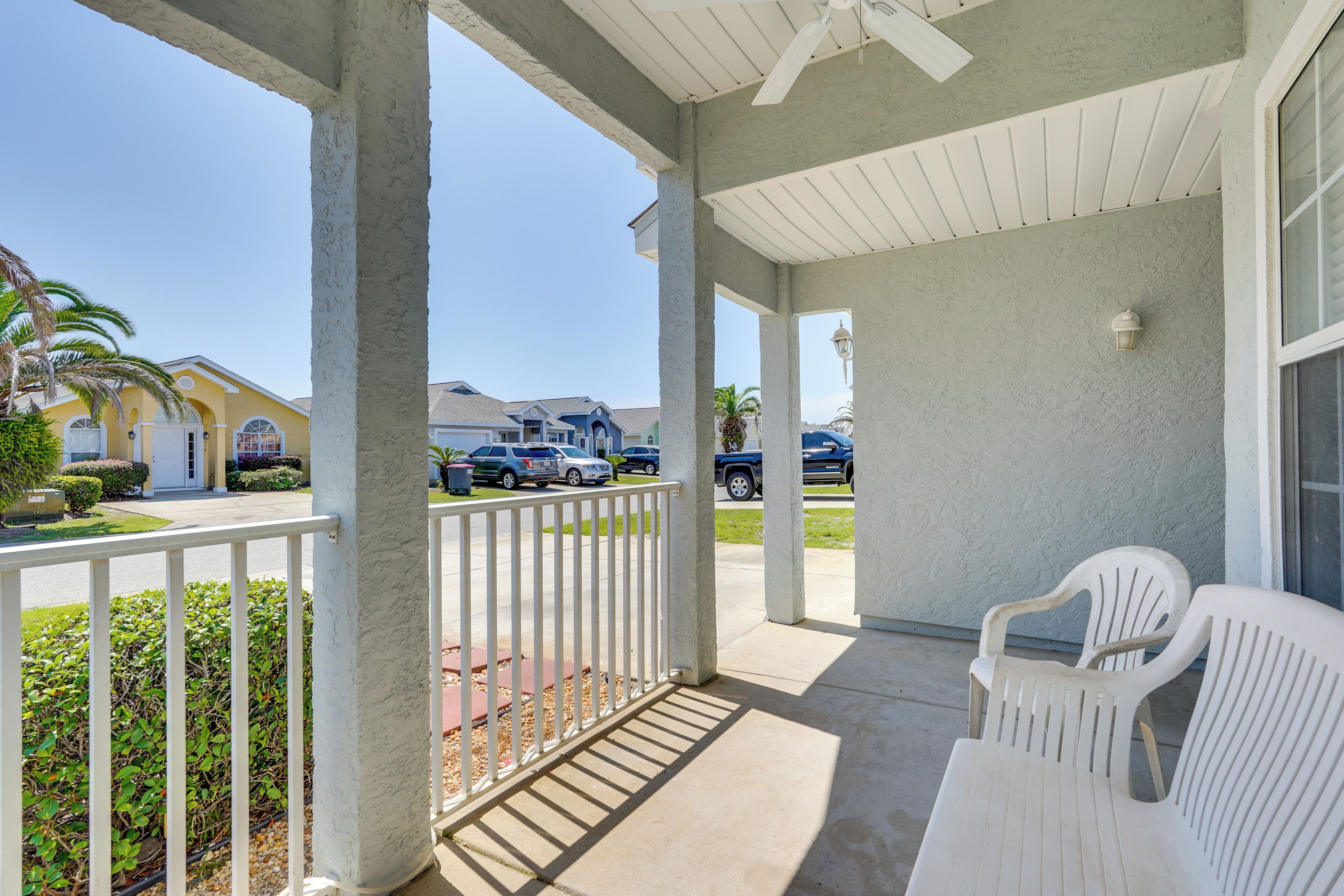 A covered outdoor area with white chairs, a concrete floor, and a view of parked cars and houses in the background.
