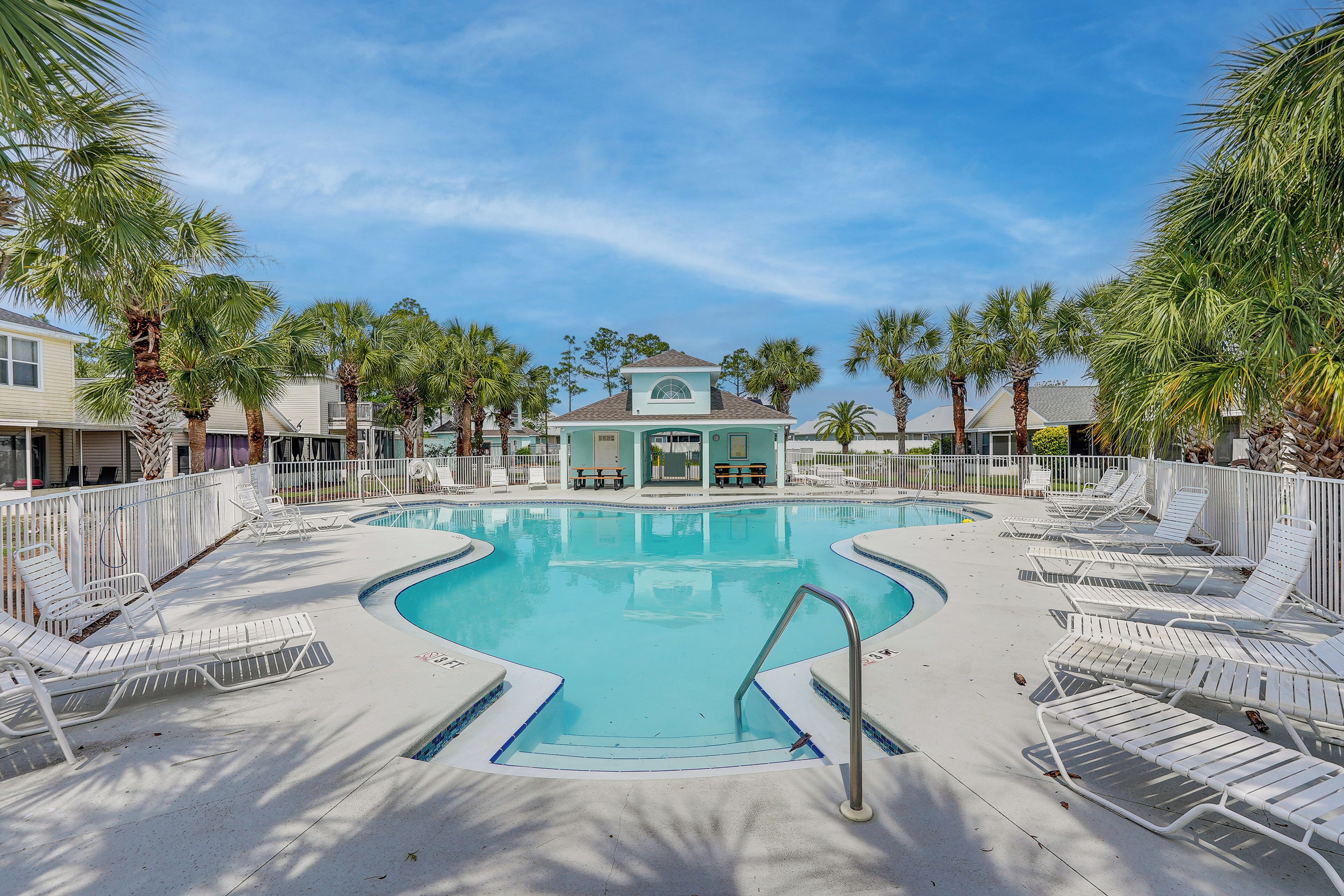 A swimming pool with lounge chairs, surrounded by palm trees and a building in the background.