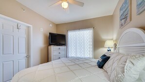 A bedroom with a bed, a television on a dresser, a ceiling fan, and a window with curtains. - Panama City Beach Condo: Balcony w/ Ocean Views! (Panama City Beach)