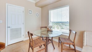 A dining area with a glass table, wicker chairs, a white door, and a window with blinds. - Panama City Beach Condo: Balcony w/ Ocean Views! (Panama City Beach)