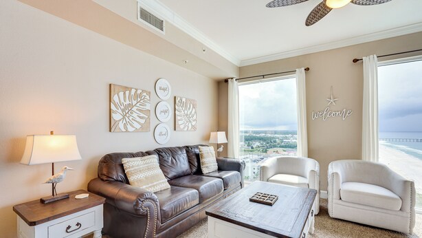 A living room with a brown leather sofa, white armchairs, a coffee table, and a view of the ocean. - Panama City Beach Condo: Balcony w/ Ocean Views! (Panama City Beach)