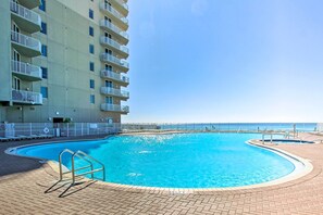 A swimming pool with a clear blue water, surrounded by a brick deck, and adjacent to a high-rise building with balconies. - Panama City Beach Condo: Balcony w/ Ocean Views! (Panama City Beach)