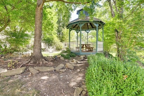 A gazebo with a bench, surrounded by trees and a garden path.