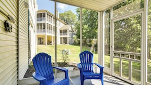 Eine überdachte Veranda mit zwei blauen Adirondack-Stühlen und einem weißen Tisch.