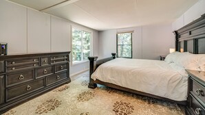 Un dormitorio con una cama grande, cómoda de madera oscura y dos ventanas que ofrecen luz natural.