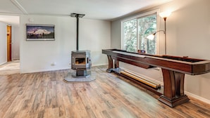 Una habitación con piso de madera, una mesa de billar, chimenea y ventana con vista a árboles.
