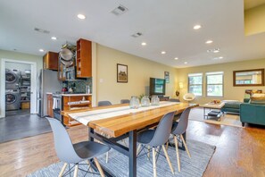 A spacious kitchen with modern appliances, a dining area with a wooden table and chairs, and a cozy living room with a green sofa and windows.
