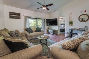 A spacious living room with a sofa set, a coffee table, a ceiling fan, and a television.