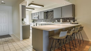 Une cuisine moderne avec des meubles gris, un grand îlot central doté de tabourets et un sol carrelé.