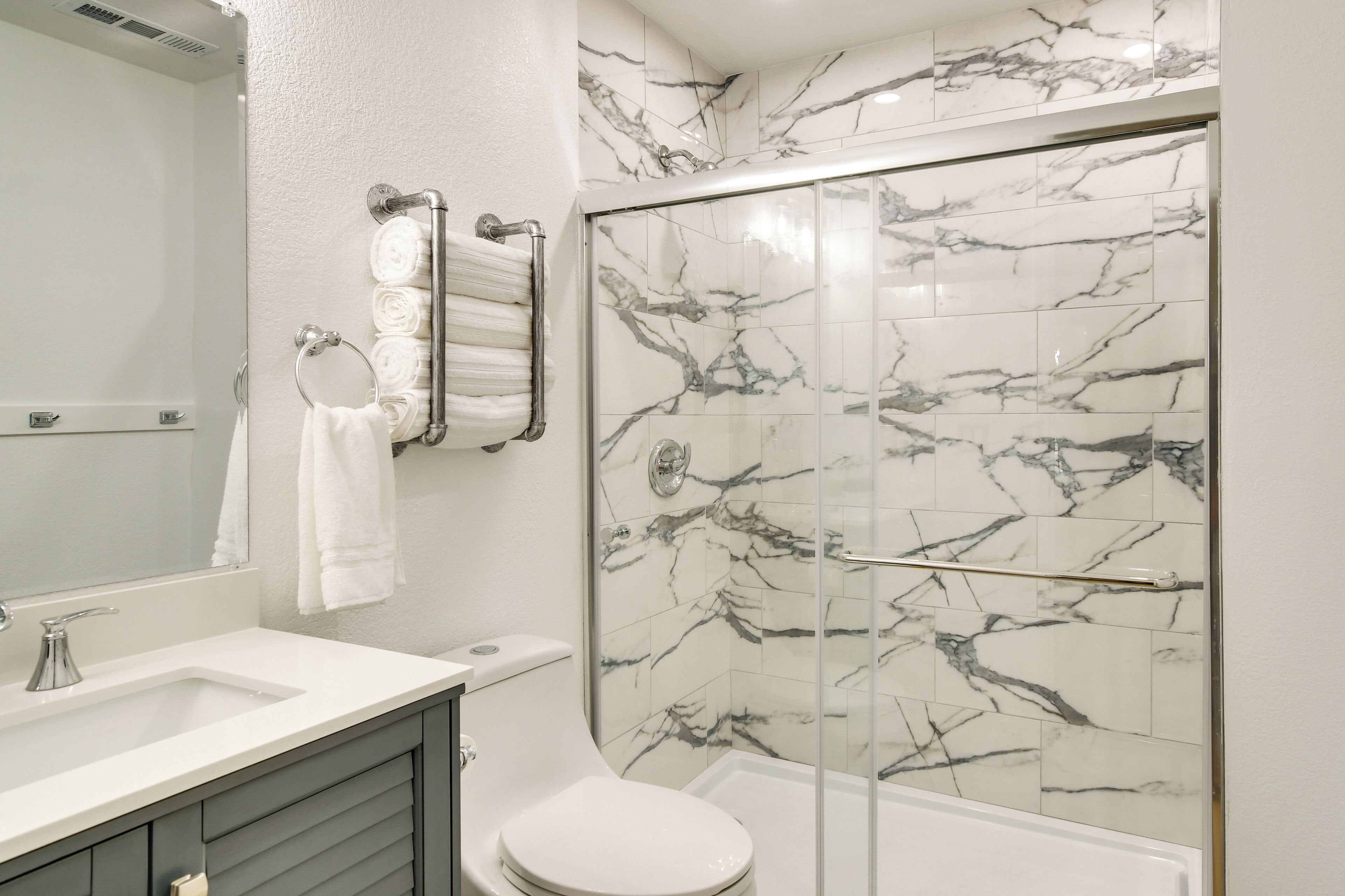 Un bagno moderno con cabina doccia in vetro, piastrelle in marmo, lavandino bianco e water.