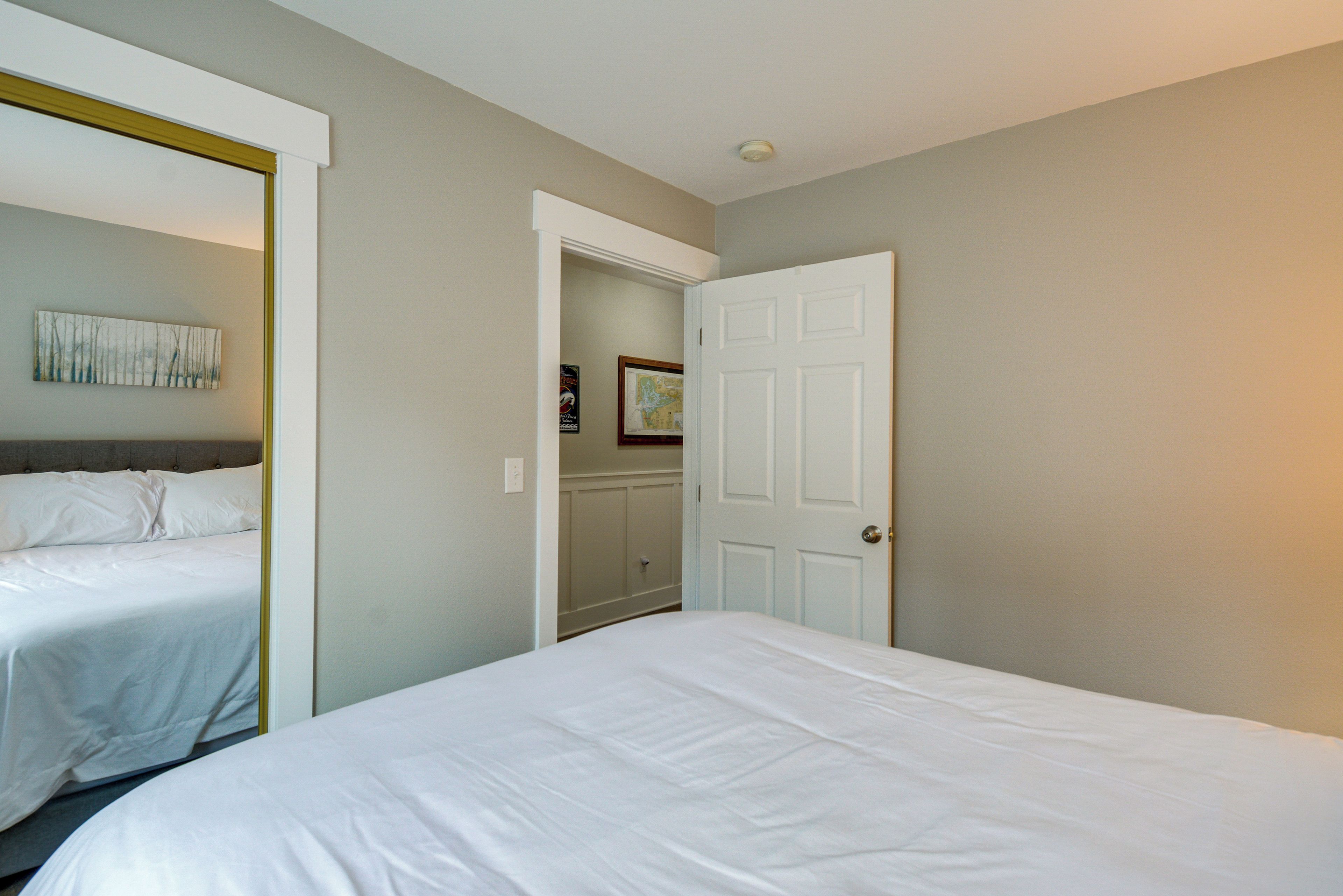 A hotel room with two beds, a door leading to a bathroom, and a small hallway with a mirror and artwork.