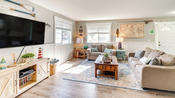 Ein Wohnzimmer mit Flachbildfernseher, einer Holz-Unterhaltungsecke, einem beige-farbenen Sofa, einem Couchtisch und einem gemusterten Teppich.