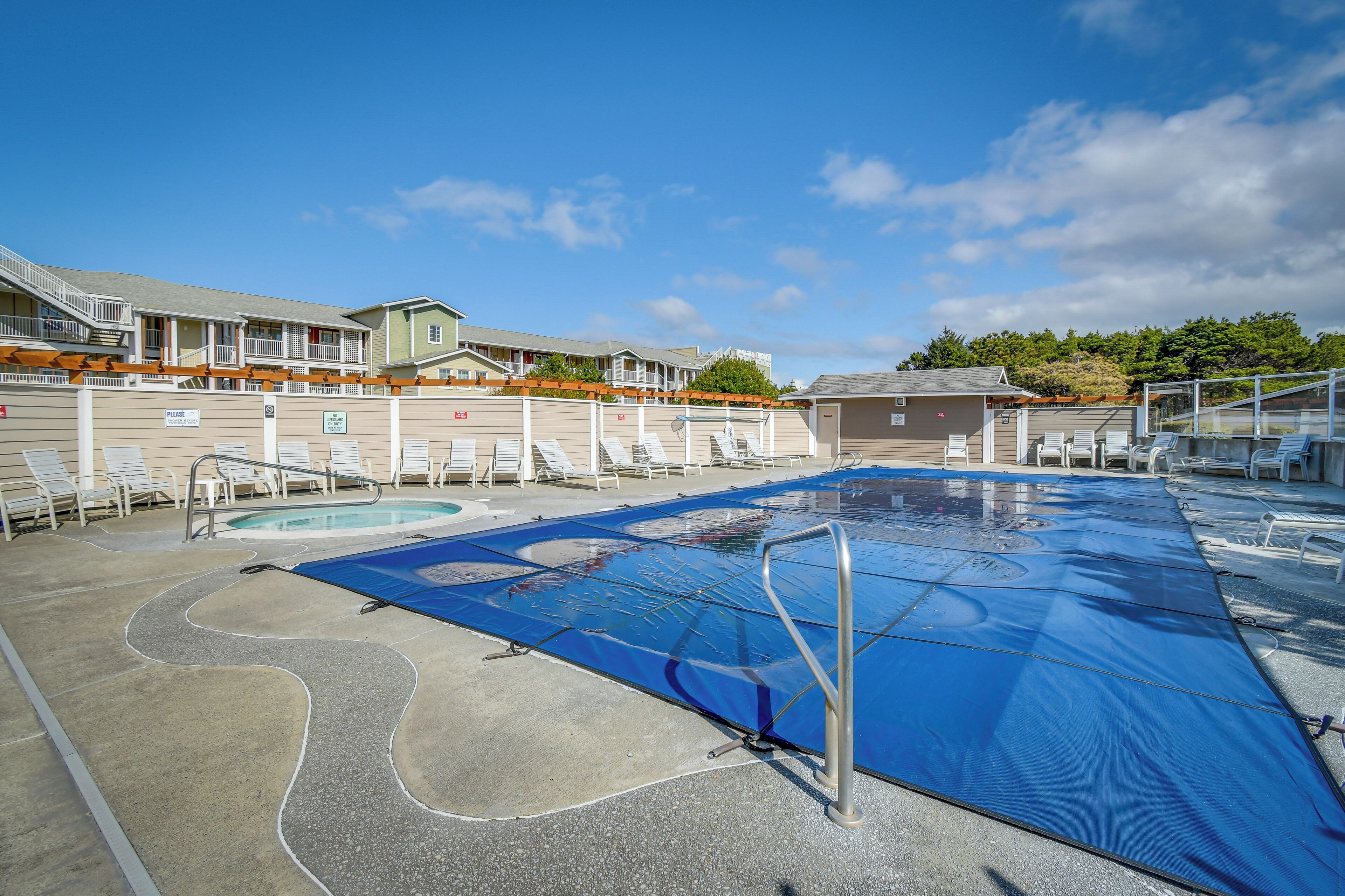 Zona de piscina amb coberta blava, gandules i un edifici amb balcons múltiples.