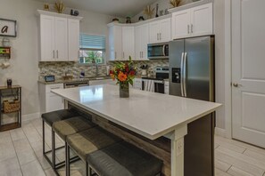 Una cocina moderna con armarios blancos, un refrigerador de acero inoxidable y una isla central con asientos.