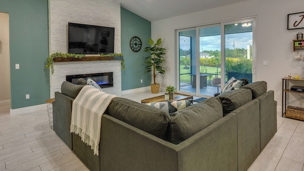 A modern living room with a sectional sofa, a fireplace, a flat-screen TV, and a large sliding glass door leading to a balcony. - Port Saint Lucie Vacation Rental w/ Hot Tub! (Port Saint Lucie)