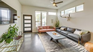 A spacious living room with a large window, a ceiling fan, a sofa, a coffee table, and a mounted animal skull. - Modern Austin Vacation Rental w/ Covered Patio (Austin)