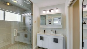 A modern bathroom with a glass-enclosed shower, a vanity with a large mirror, and a light fixture above the mirror. - Modern Austin Vacation Rental w/ Covered Patio (Austin)