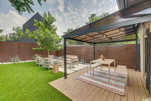 A covered patio area with outdoor furniture, a wooden deck, and a grassy lawn. - Modern Austin Vacation Rental w/ Covered Patio (Austin)