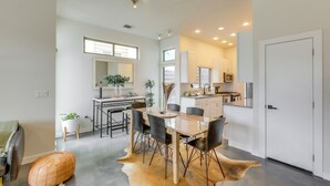 A modern kitchen with white cabinets, a dining area with a glass table, and a living space with a leather pouf. - Modern Austin Vacation Rental w/ Covered Patio (Austin)