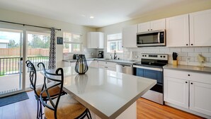 A modern kitchen with white cabinets, a large island, stainless steel appliances, and a view to the outside.