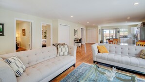 A spacious living area with two sofas, a coffee table, and a rug. There is a dining area with a table and chairs visible in the background.