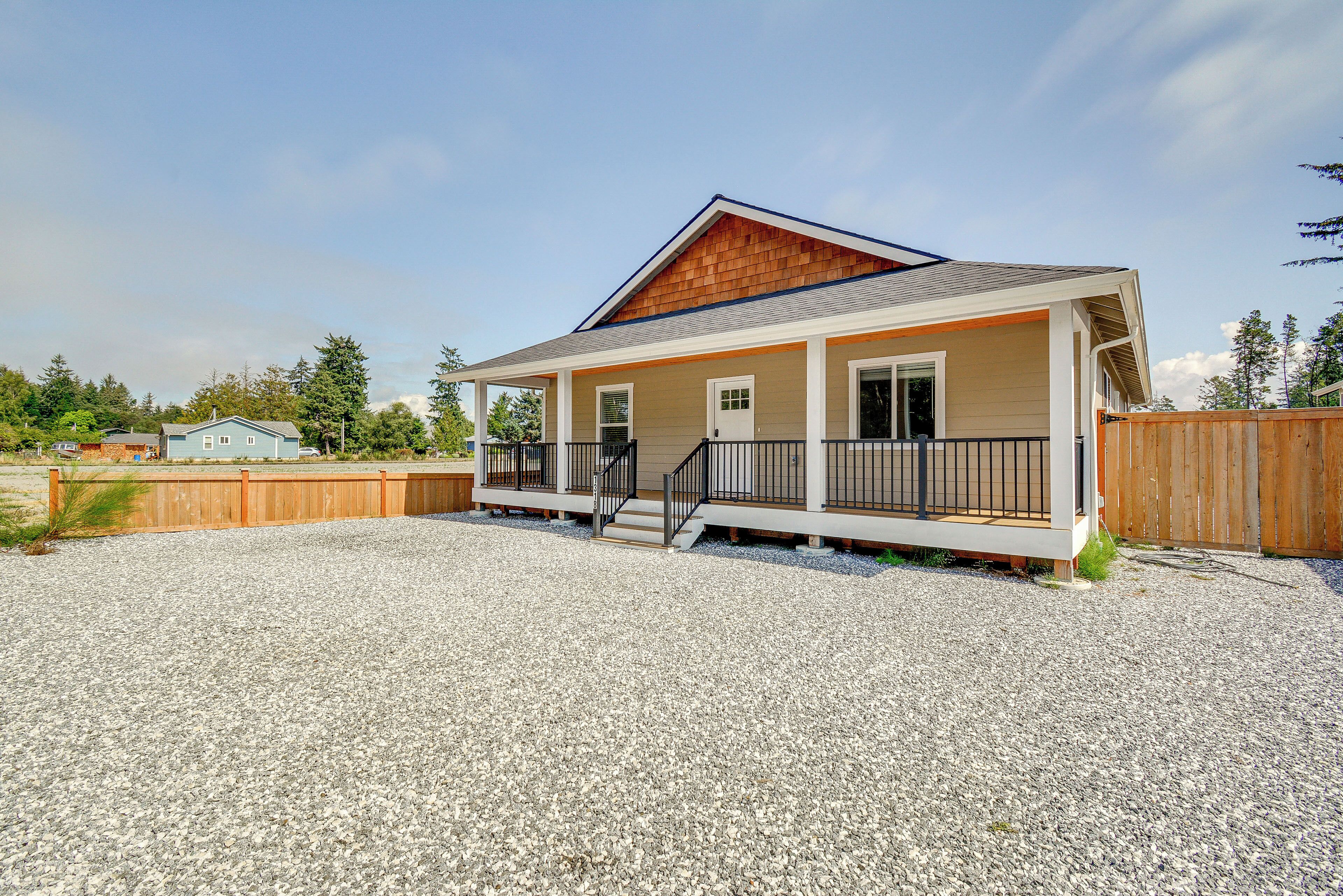A single-story house with a porch, a wooden deck, and a gravel driveway.