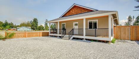 A single-story house with a porch, a wooden deck, and a gravel driveway.