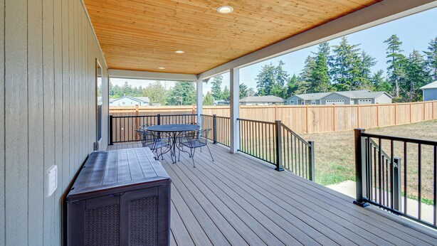 A covered outdoor deck with a wooden ceiling, a table and chairs, and a grill.