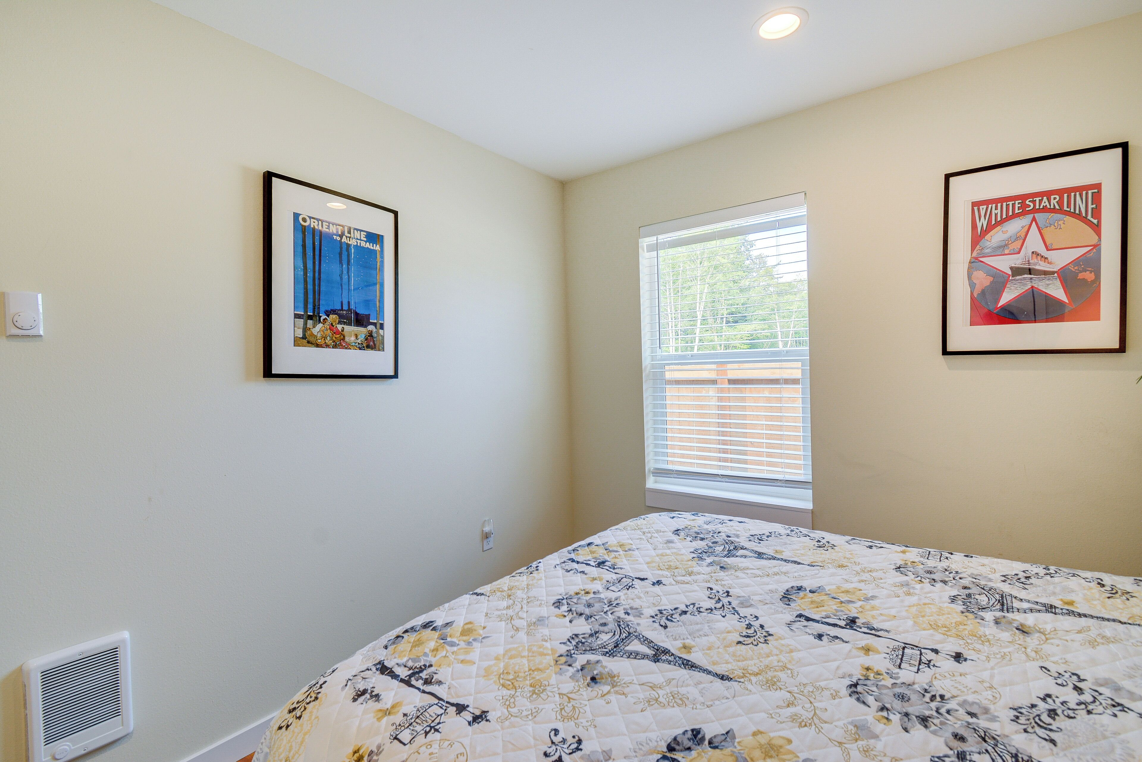 A bedroom with a bed, a window with blinds, and two framed pictures on the wall.