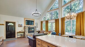 A spacious kitchen with a large island, wooden cabinets, and a stone fireplace. There are large windows with curtains, a cozy seating area, and a television mounted on the wall. - Unwind in Cle Elum: Hot Tub & Cozy Fireplace! (Cle Elum)