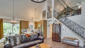 A spacious living area with a leather sofa, a wooden coffee table, and a chandelier. A staircase with a metal railing leads to an upper level. - Unwind in Cle Elum: Hot Tub & Cozy Fireplace! (Cle Elum)
