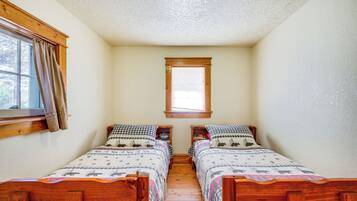 A small, cozy room with two wooden beds, a window with curtains, and a wooden ceiling.