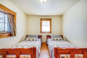 A small, cozy room with two wooden beds, a window with curtains, and a wooden ceiling.