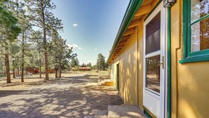 A wooden cabin with a large window and a door, surrounded by trees and a dirt path. - Secluded Stonewall Cabin w/ Mountain View! (Weston)
