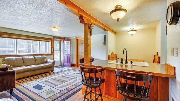 A cozy living room with a sofa, a patterned rug, and wooden chairs. - Secluded Stonewall Cabin w/ Mountain View! (Weston)