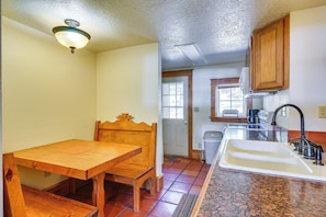 A kitchen with a wooden table and chairs, a sink, and cabinets. - Secluded Stonewall Cabin w/ Mountain View! (Weston)