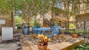 An outdoor patio area with a wooden table and chairs, a potted plant, and a staircase leading to an upper level.