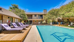 A pool area with lounge chairs, a wooden deck, and a building with multiple balconies.