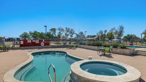 Una piscina con jacuzzi, rodeada por un patio de ladrillo y muebles de exterior.