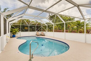 An indoor swimming pool with a glass ceiling, surrounded by lounge chairs and potted plants.