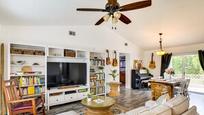 A living room with a TV, bookshelves, guitars, a dining area, and a ceiling fan. - Port St Lucie Oasis w/ Heated Saltwater Pool! (Port Saint Lucie)